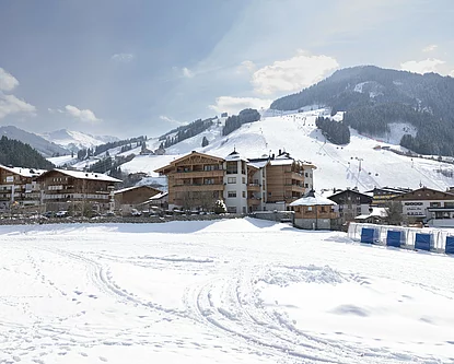 Winterliche Aussenansicht des Hotels Unterschwarzachhofs in Saalbach Hinterglemm, umgeben von verschneiten Bergen.