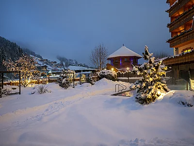 Winterliche Abendstimmung der Outdoor-Wellnessbereich & Pool vom Skihotel der Unterschwarzachhof in Saalbach Hinterglemm mit tiefverschneiter Landschaft.