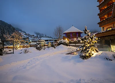 Winterliche Abendstimmung der Outdoor-Wellnessbereich & Pool vom Skihotel der Unterschwarzachhof in Saalbach Hinterglemm mit tiefverschneiter Landschaft.