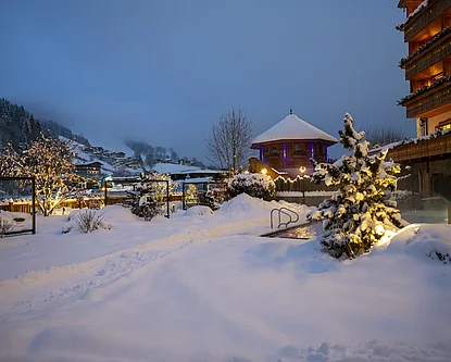 Winterliche Abendstimmung der Outdoor-Wellnessbereich & Pool vom Skihotel der Unterschwarzachhof in Saalbach Hinterglemm mit tiefverschneiter Landschaft.
