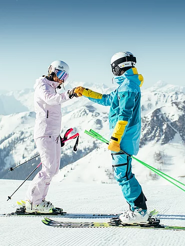Zwei Skifahrer stoßen mit Fäusten an auf sonniger Piste im Skicircus Saalbach Hinterglemm Leogang Fieberbrunn