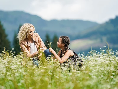 Mutter und Tochter sitzen auf der Wiese beim Hotel Unterschwarzachhof in Saalbach Hinterglemm