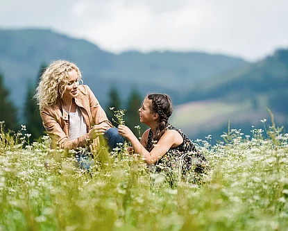 Mutter und Tochter sitzen auf der Wiese beim Hotel Unterschwarzachhof in Saalbach Hinterglemm