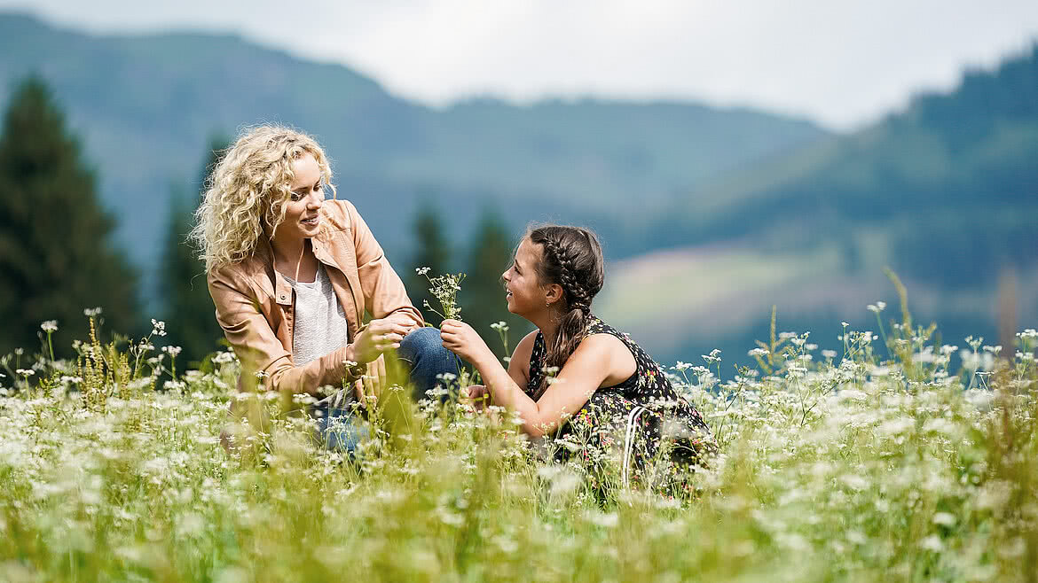 Mother and daughter sitting on the meadow at the Hotel Unterschwarzachhof in Saalbach Hinterglemm