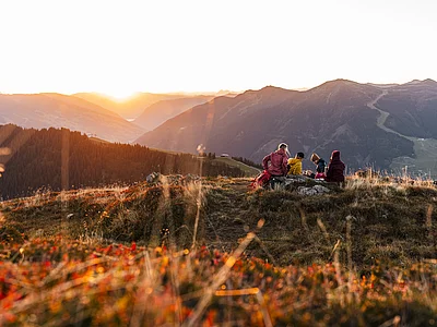 Wanderer sitzen auf einem Stein im Sonnenaufgang im Herbst in Saalbach Hinterglemm