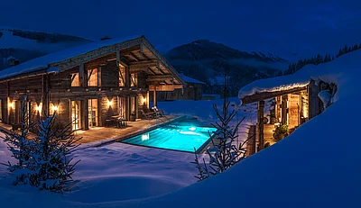Beleuchtetes Chalet die Schmiedalm im Schnee mit Außenpool und Bergkulisse bei Nacht.