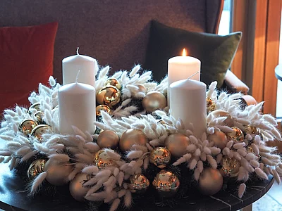 Adventskranz aus weißen Gräsern mit weißen Kerzen, goldenen Kugeln - eine Kerze brennt